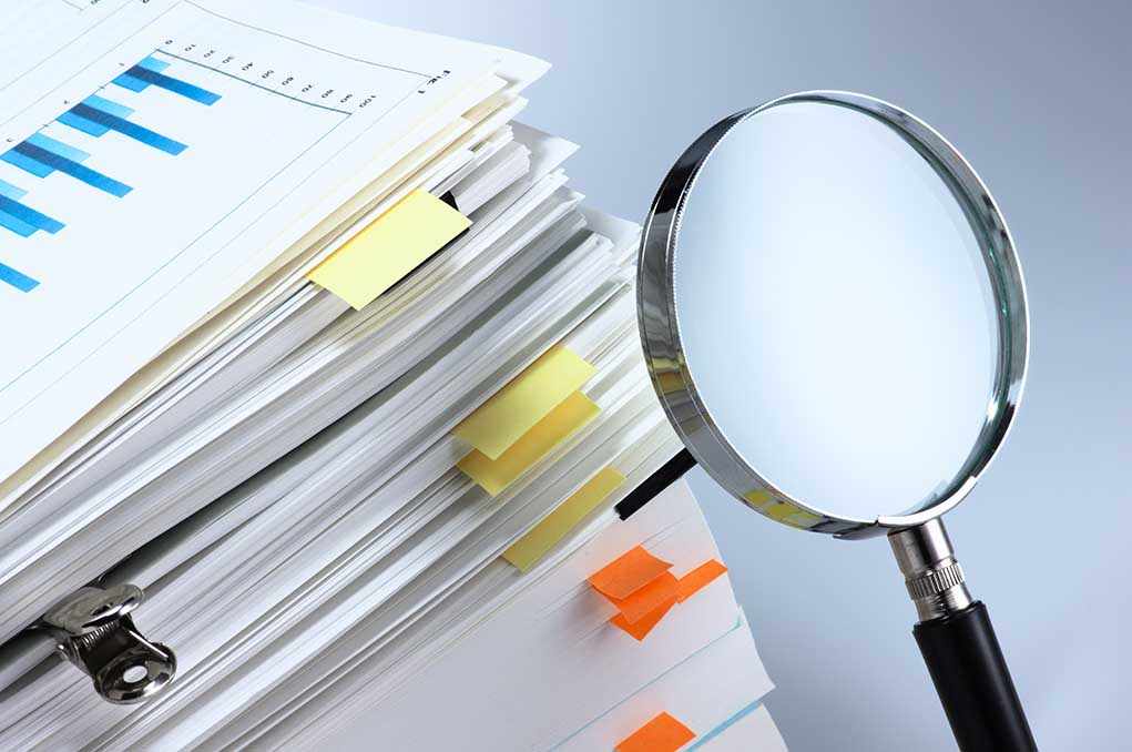 Stack of documents with a magnifying glass beside it