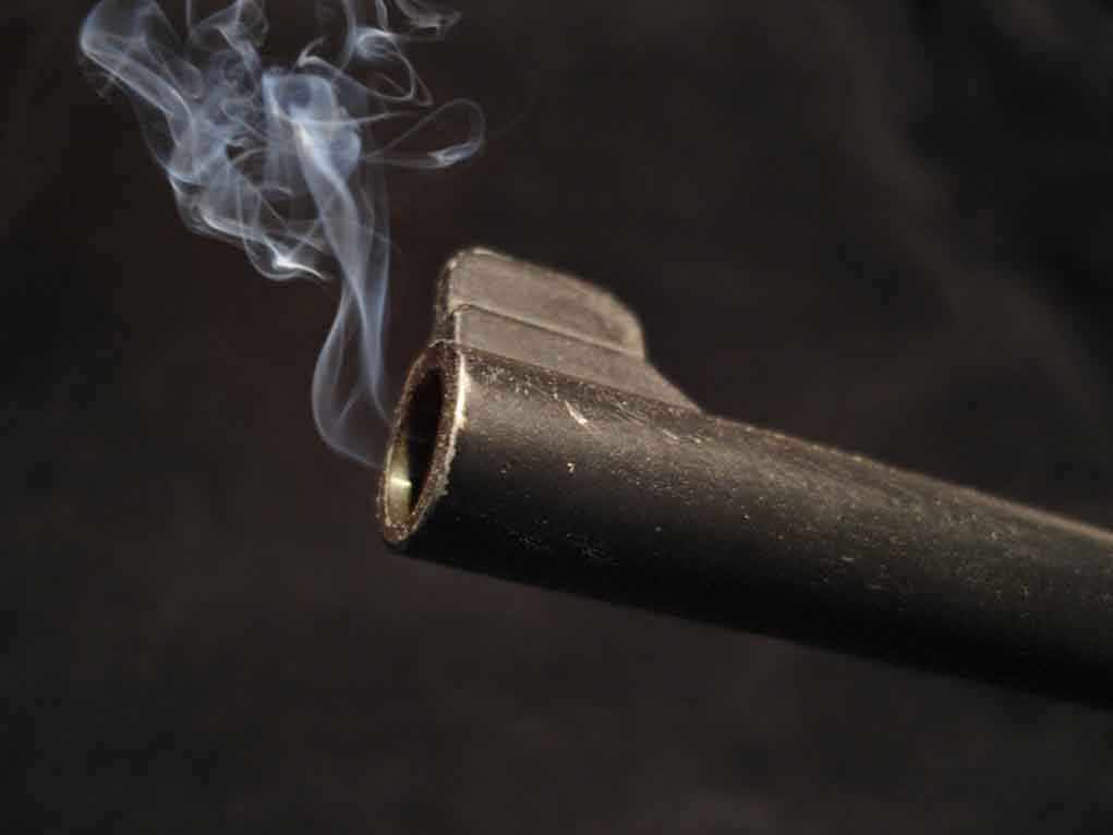 shutterstock_4250866.jpg Close-up of a gun barrel emitting smoke against a black background