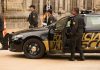 Police officers standing and sitting near a patrol car.