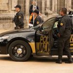 Police officers standing and sitting near a patrol car.