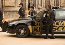 Police officers standing and sitting near a patrol car.