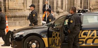 Police officers standing and sitting near a patrol car.