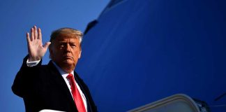 A political figure waving while standing on the steps of an aircraft