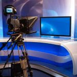 TOP News Anchor BUSTED – Massive Scam EXPOSED TV studio with camera and empty anchor desk.