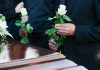 Mourners holding white roses by a casket.