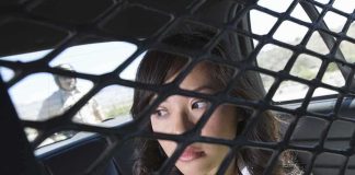 A woman sitting in the back of a police car, looking through a protective mesh barrier