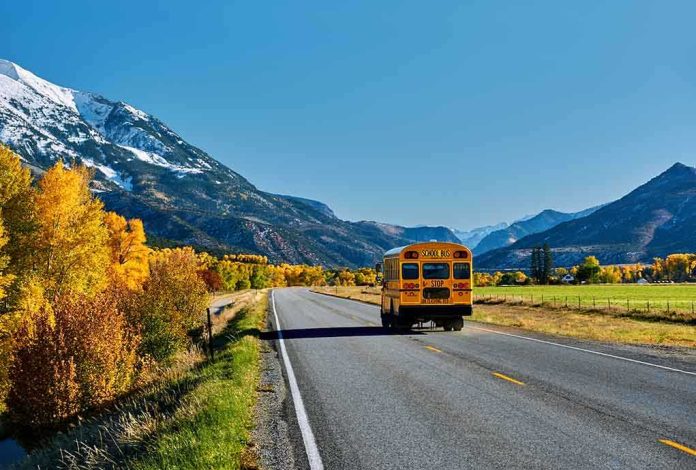 shutterstock_1151523266.jpg A yellow school bus driving on a rural road surrounded by autumn trees and mountains