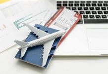A model airplane on a blue passport next to a laptop and boarding pass