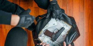 Gloved hands around bag with money and gun.