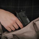 Hand placing handgun into beige handbag.