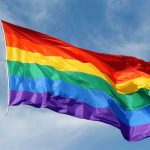 A rainbow flag waving against a blue sky