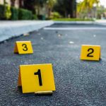 Repeat Offender FREED – Doctor Brutally Attacked! Crime scene markers on asphalt with bullet casing.