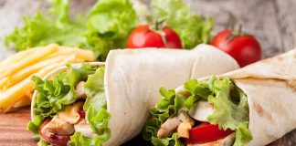 Two chicken wraps filled with lettuce and tomatoes on a wooden plate with fries