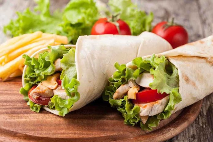 shutterstock_223409203.jpg Two chicken wraps filled with lettuce and tomatoes on a wooden plate with fries