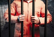 TV Star MURDERS Cellmate Behind Bars Person in an orange jumpsuit gripping prison bars in a dark cell