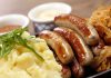 Sausages, mashed potatoes, sauerkraut, and sauces on plate.