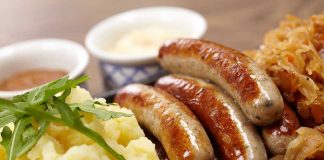 Sausages, mashed potatoes, sauerkraut, and sauces on plate.