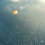 Orange hot air balloon above a town in fog.