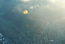 Orange hot air balloon above a town in fog.
