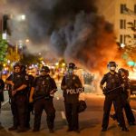 Dark Money Web Fuels Minneapolis Protests Police officers in riot gear near burning car.
