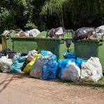 Overflowing garbage bins with bags on the ground.