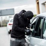 Person in black breaking into a car.