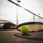 Tennis racket and ball on court near net.