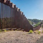 Mexico REFUSES U.S. Military – Shocking Power Play Tall metal border wall with rural landscape.