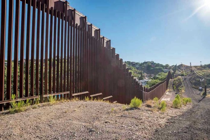 657897121 Tall metal border wall with rural landscape.