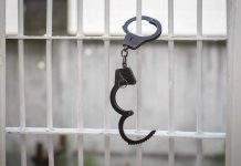 Murder Accomplice Seeks Early Freedom Handcuffs hanging on white metal bars.