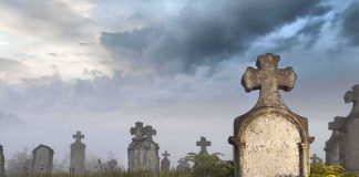 Foggy graveyard with tombstones and crosses under a cloudy sky