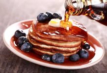 Stack of pancakes topped with butter and blueberries, drizzled with maple syrup