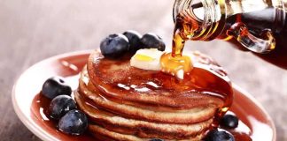 Stack of pancakes topped with butter and blueberries, drizzled with maple syrup