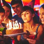 Group of friends celebrating a birthday with a cake and drinks