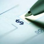 Turning Point USA PLEDGES Trump Account Match Close-up of a pen poised over a check with a dollar sign