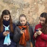 Sweden BANS Phones After Education Collapse Three teenagers using smartphones while standing against a textured wall