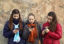 Sweden BANS Phones After Education Collapse Three teenagers using smartphones while standing against a textured wall