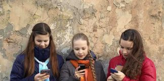Three teenagers using smartphones while standing against a textured wall
