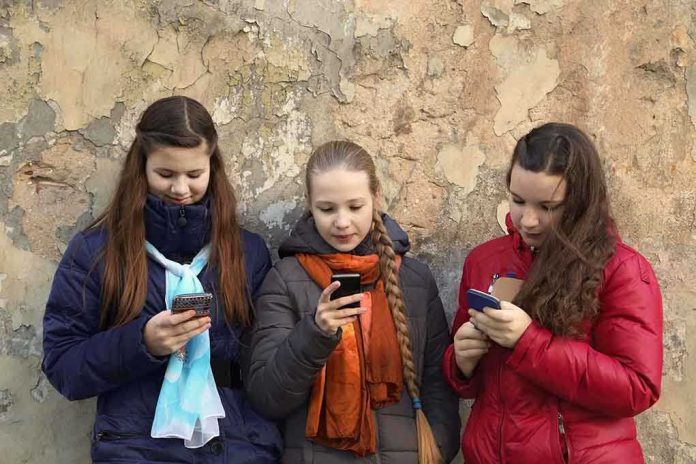 shutterstock_234224188.jpg Three teenagers using smartphones while standing against a textured wall