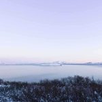 Two Teens PLUNGE Into Frozen Pond A serene winter landscape featuring a calm lake surrounded by snow-covered mountains under a twilight sky