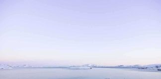 A serene winter landscape featuring a calm lake surrounded by snow-covered mountains under a twilight sky