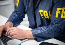 FBI Knocked, Dad Ignored—Four People DEAD Person in FBI jacket typing on a laptop.