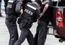 Rock Attack Turns Protest Into Felony Police officers arresting a handcuffed person.