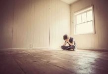 A child sitting alone in an empty room, covering their face with their hands