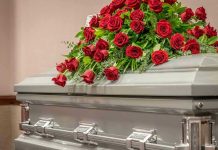 Governor Slashes ICE—Mom Pays Ultimate Price Silver casket with red rose arrangement on top.