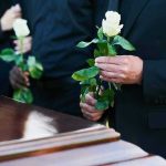Mourners holding white roses by a casket.