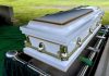 White casket on a lowering device at gravesite.