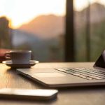 Laptop, coffee cup, and phone on wooden table.