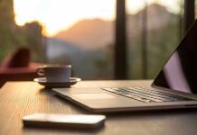 Laptop, coffee cup, and phone on wooden table.