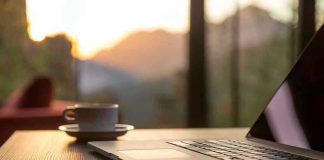 Beloved Café Owner VANISHES Midday Laptop, coffee cup, and phone on wooden table.